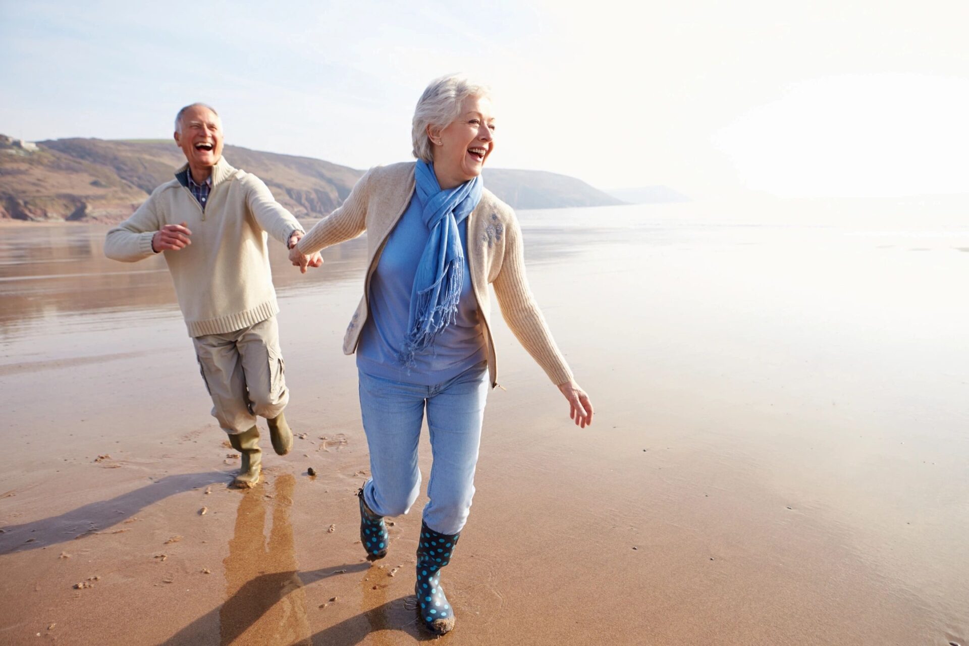 A man and woman holding hands while walking on the beach.